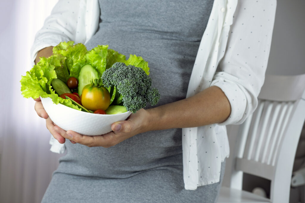 Pregnant woman with bowl of fresh vegetables, broccoli, leaf salad, tomato.